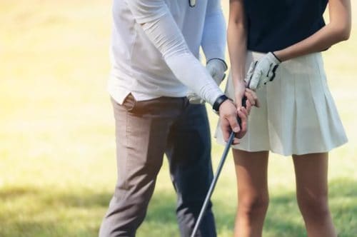 a male coach showing a rookie female golfer how to hold a wood 