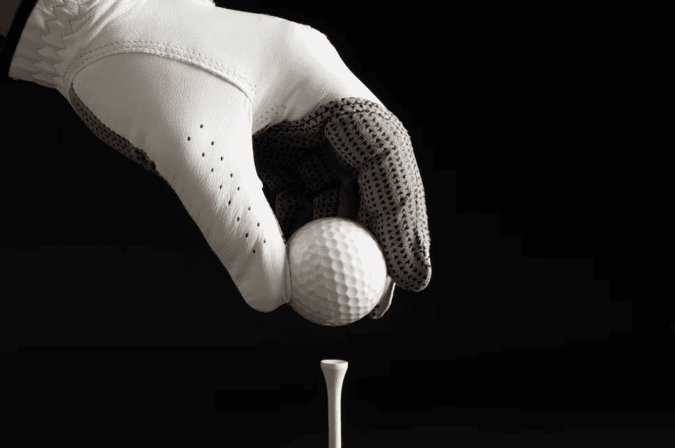 hand in gloves holds the golf ball on black background 