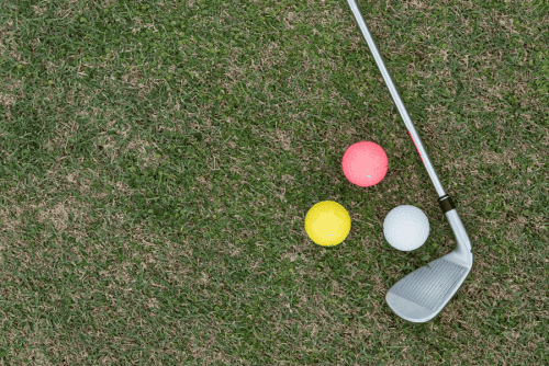 Three different golf ball colors and a club resting on the grass