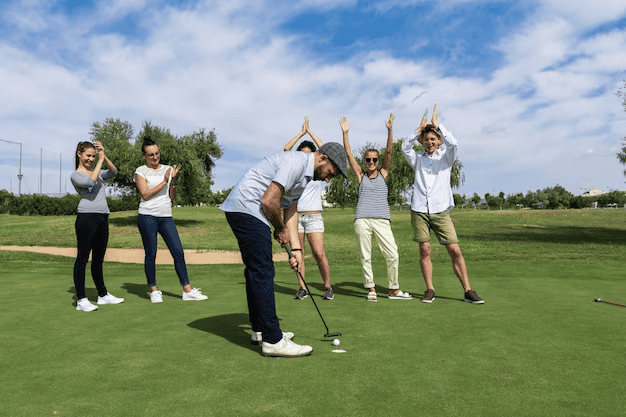 people on a golf course, one taking turns to strike the ball while the rest cheer on