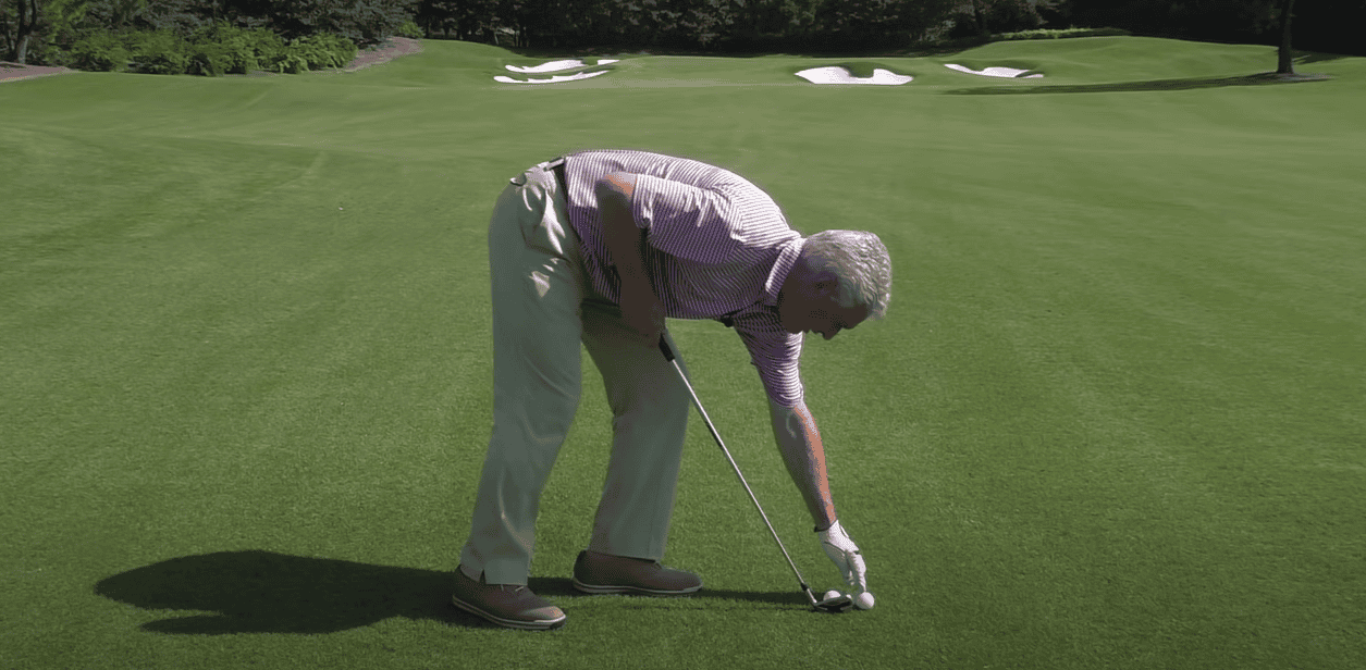 man with a golf club, tapping a golf ball on the grass at the golf course