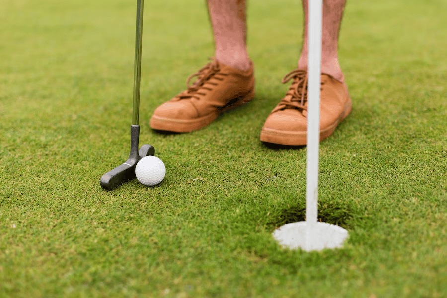 Man wearing Brown Shoes with Golf Club, Ball, and Hole Close By