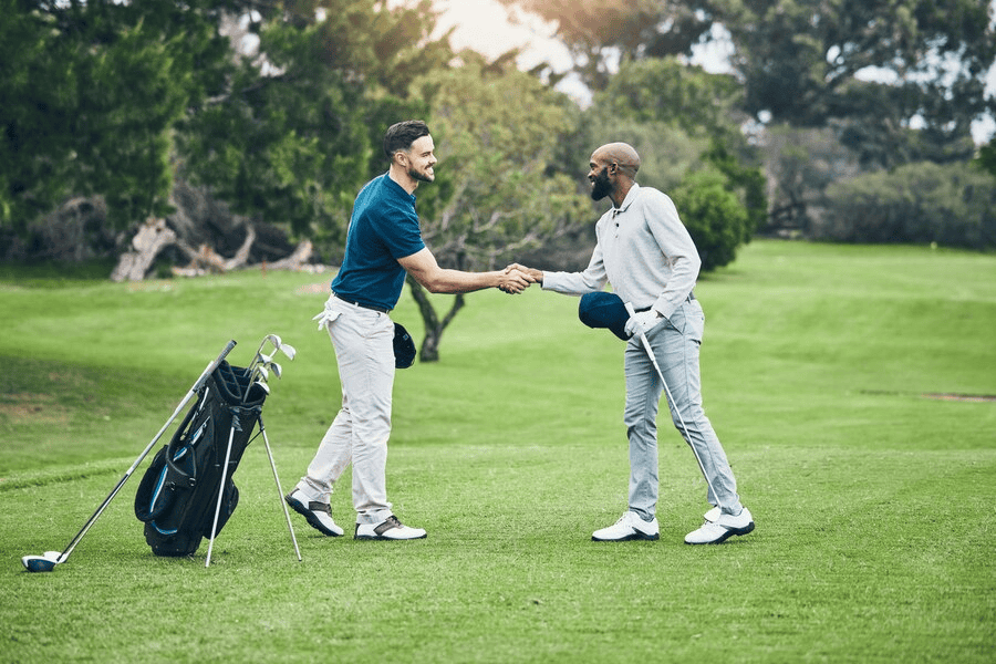 Two men shaking hands on a golf course, with a golf bag