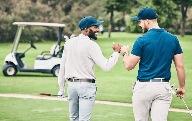 Two men chatting while walking on a golf course, with a noticeable golf cart nearby