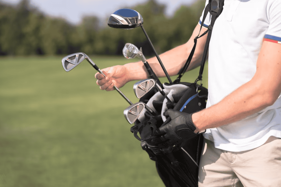 Man in white t-shirt and beige pants removing a golf club from his golf bag
