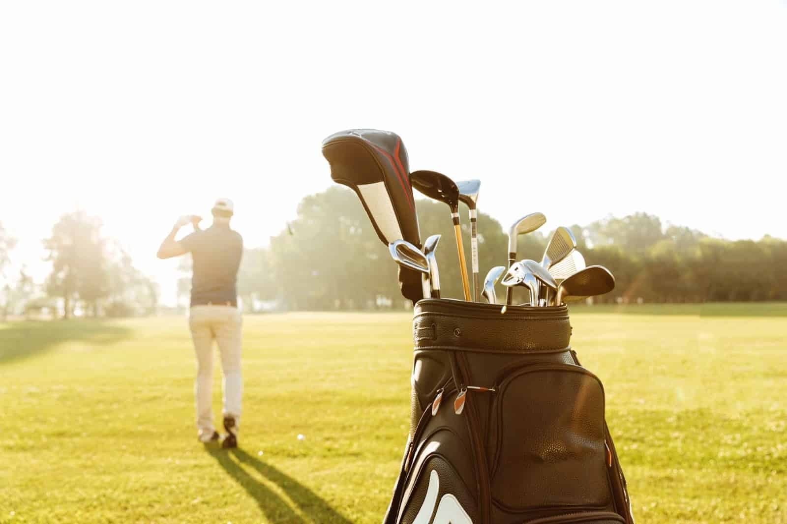 a golf bag with clubs and a male golfer swinging a club in the field